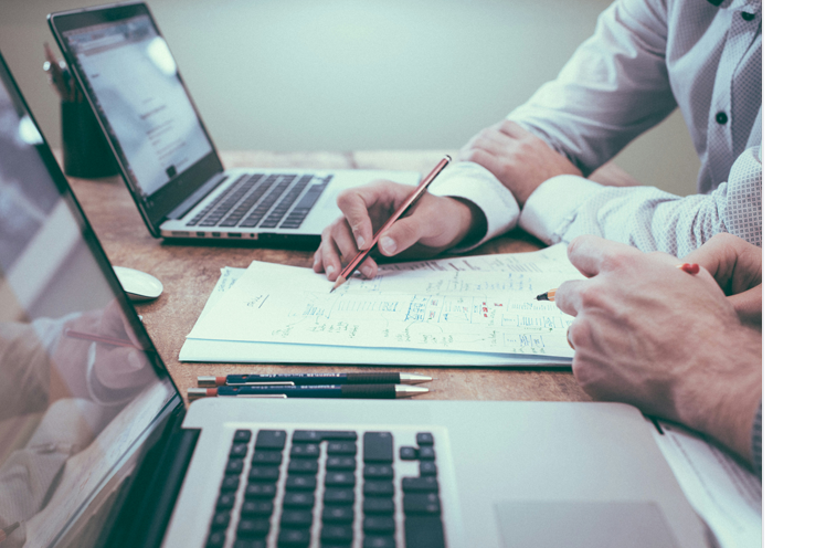 un agente inmobiliario entre ordenadores y papeles, explicando a su cliente los servicios que ofrece inmobiliaria Servicasa para los vendedores de propiedades